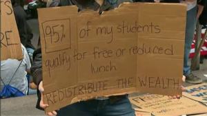 Un manifestant tient une pancarte sur laquelle est affiché que 95% de ses élèves sont éligibles aux repas gratuits de l'État